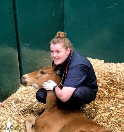 Lucy Lamont, equine vet, kneeling with a foal on a bed of wood shavings
